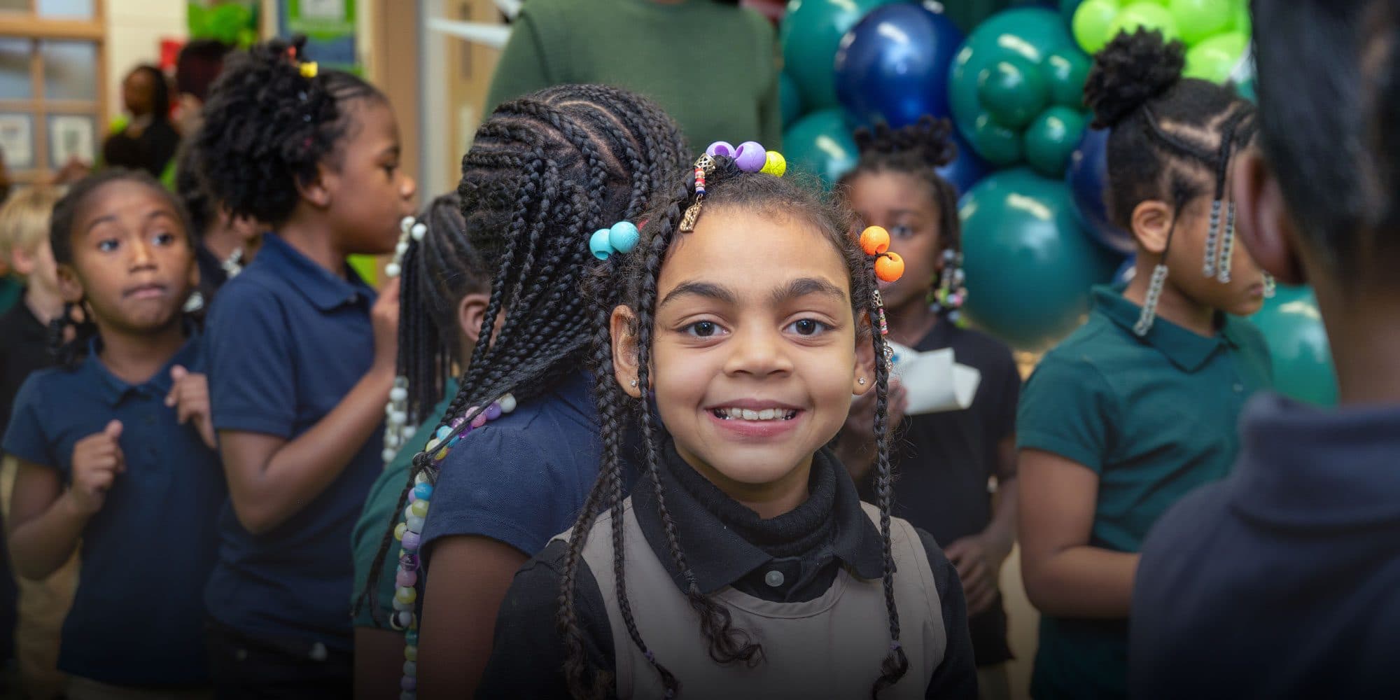 Smiling student with beaded braids standing among classmates.