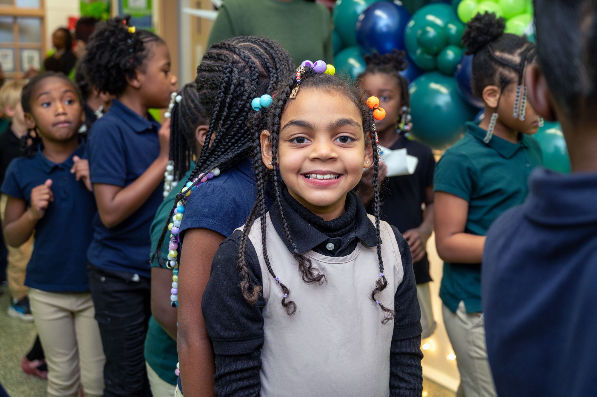 Smiling student with beaded braids in a line of classmates.